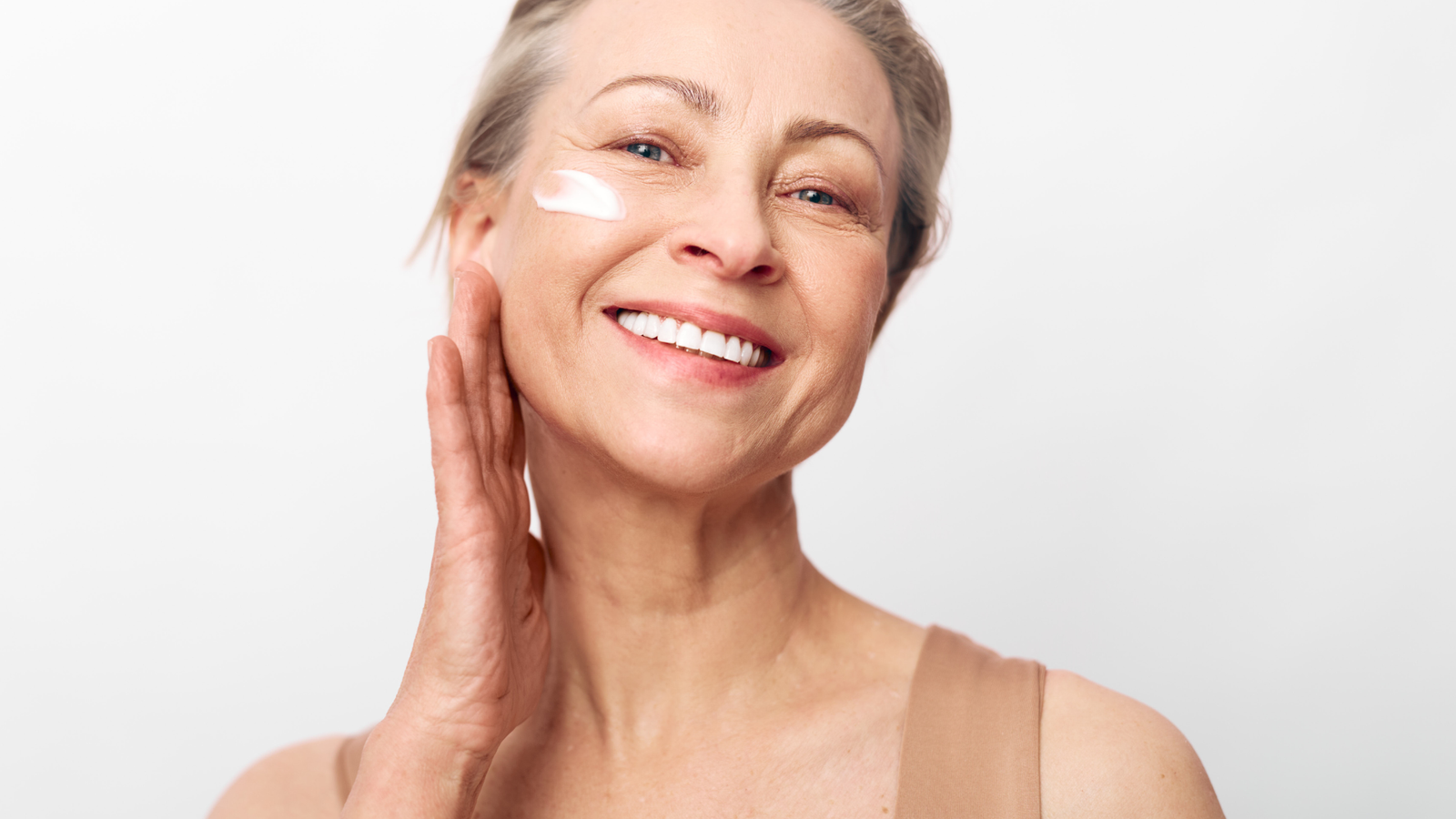 Mature woman applying facial moisturizer illustrating peptides vs collagen for reducing wrinkles, improving skin firmness, boosting hydration, and supporting healthy aging.